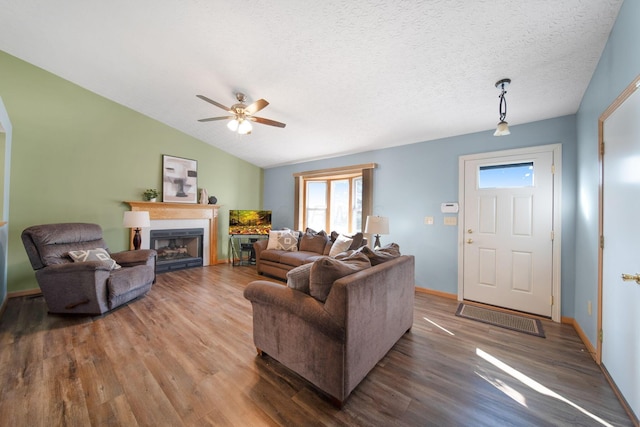 living room featuring a ceiling fan, a textured ceiling, wood finished floors, a fireplace, and lofted ceiling