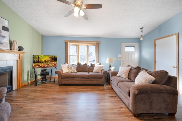 living room featuring a fireplace, a textured ceiling, a ceiling fan, and wood finished floors