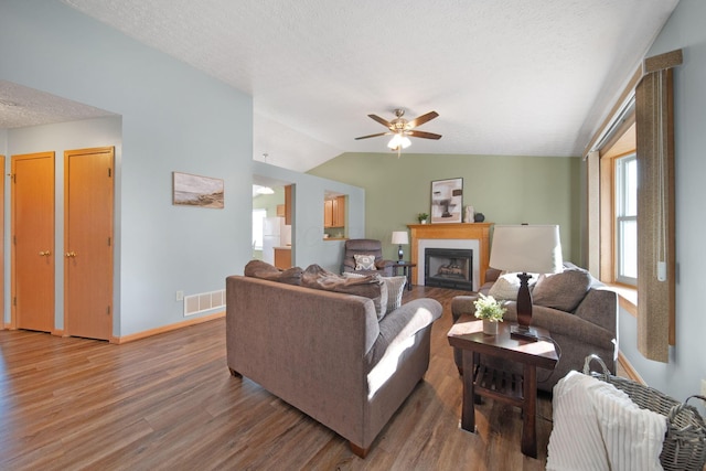 living room featuring wood finished floors, visible vents, a fireplace, vaulted ceiling, and a textured ceiling