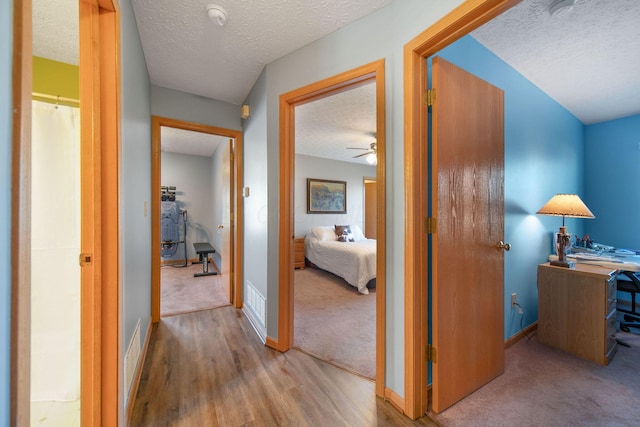 corridor with baseboards, a textured ceiling, carpet floors, and wood finished floors