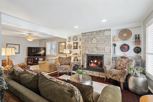 living room featuring a ceiling fan, built in features, wood finished floors, recessed lighting, and a stone fireplace