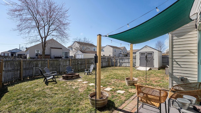 view of yard featuring a fire pit, a shed, a residential view, a fenced backyard, and an outbuilding