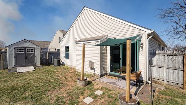 rear view of house with an outdoor structure, cooling unit, a fenced backyard, and a lawn