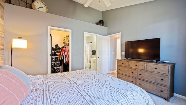 bedroom featuring a ceiling fan, baseboards, ensuite bath, a spacious closet, and light carpet