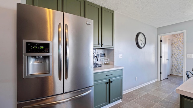 kitchen featuring stainless steel refrigerator with ice dispenser, a textured ceiling, green cabinets, light countertops, and baseboards