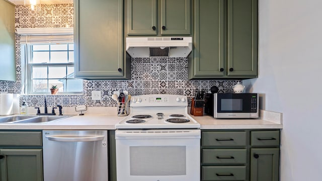 kitchen with a sink, under cabinet range hood, stainless steel appliances, green cabinets, and light countertops