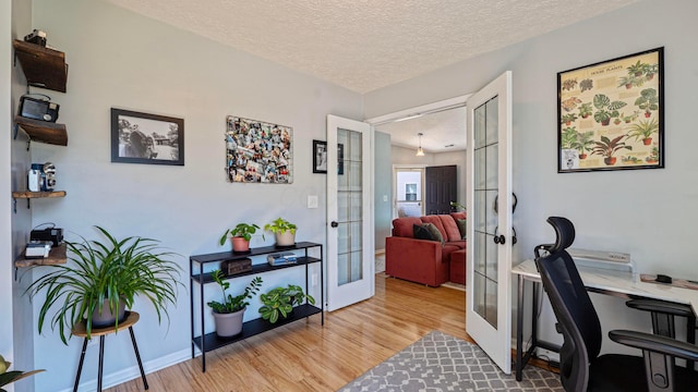 office featuring light wood finished floors, french doors, a textured ceiling, and baseboards