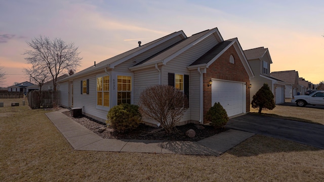 view of side of property featuring brick siding, central air condition unit, a lawn, a garage, and driveway