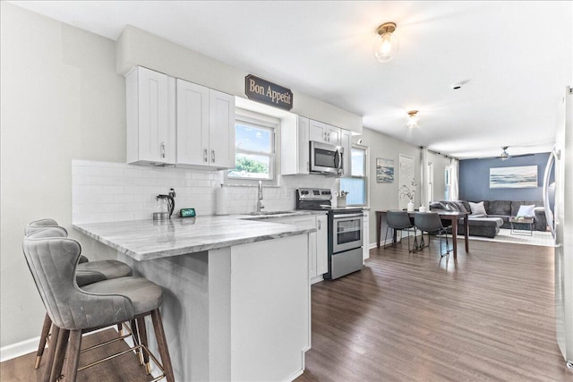 kitchen with decorative backsplash, a breakfast bar, stainless steel appliances, a sink, and white cabinetry