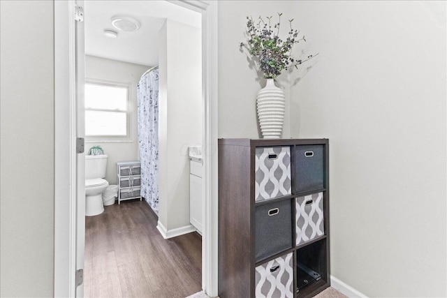bathroom with wood finished floors, toilet, a shower with shower curtain, and baseboards