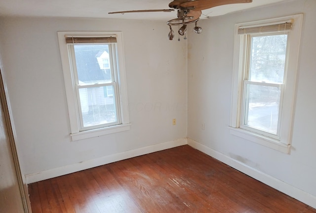 unfurnished room with dark wood finished floors, a healthy amount of sunlight, a ceiling fan, and baseboards