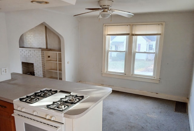 kitchen featuring visible vents, a peninsula, gas range gas stove, ceiling fan, and a brick fireplace