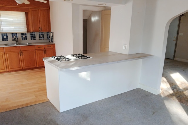 kitchen featuring brown cabinetry, cooktop, decorative backsplash, arched walkways, and a sink