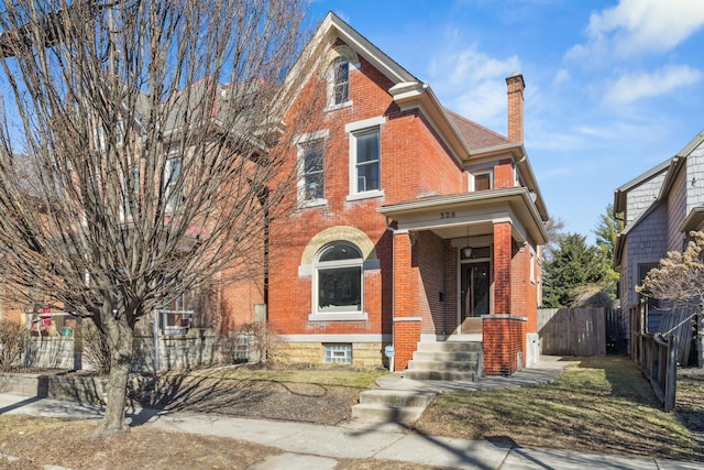 view of front of house with brick siding, a chimney, and fence