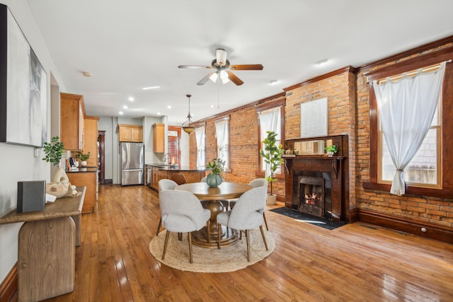 dining space featuring a ceiling fan, a large fireplace, brick wall, light wood finished floors, and baseboards