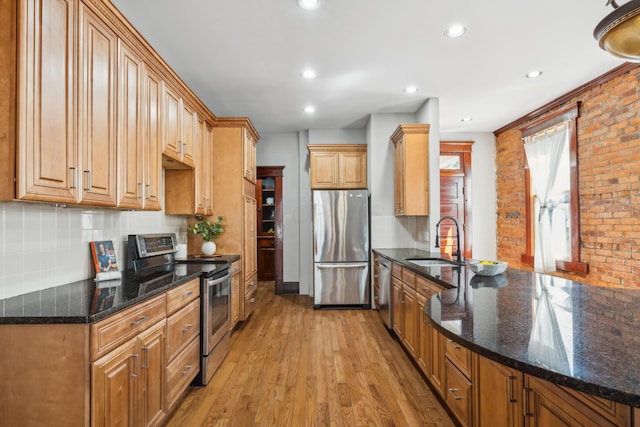 kitchen with light wood finished floors, tasteful backsplash, appliances with stainless steel finishes, a peninsula, and a sink