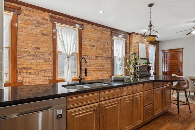 kitchen with dark stone countertops, brick wall, a sink, dark wood-type flooring, and stainless steel dishwasher