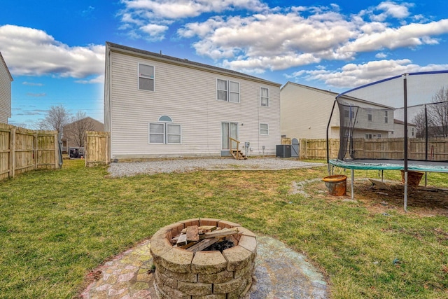 back of property featuring a trampoline, an outdoor fire pit, a lawn, a fenced backyard, and a patio area