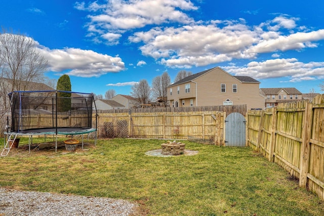 view of yard with a trampoline, a fenced backyard, a residential view, and an outdoor fire pit