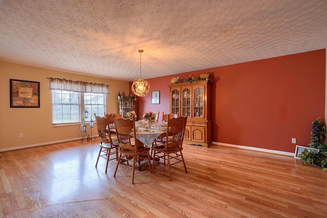 dining space featuring an inviting chandelier, baseboards, light wood-type flooring, and a textured ceiling