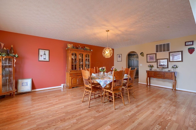 dining area featuring baseboards, visible vents, arched walkways, light wood-style floors, and a textured ceiling