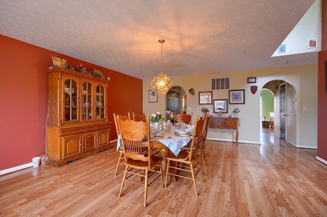 dining space featuring visible vents, arched walkways, a textured ceiling, and light wood finished floors