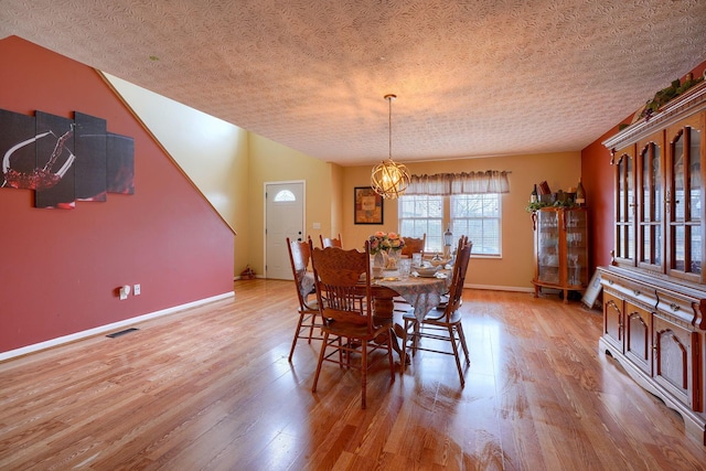 dining space with visible vents, baseboards, wood finished floors, a notable chandelier, and a textured ceiling