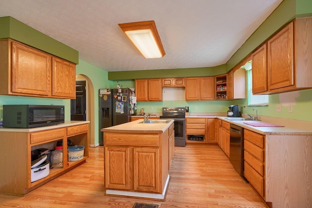 kitchen featuring a kitchen island with sink, open shelves, arched walkways, stainless steel appliances, and a sink