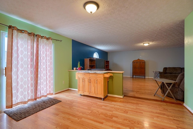 kitchen with open floor plan, light wood-style flooring, a textured ceiling, and baseboards