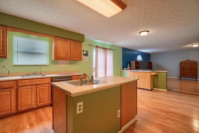 kitchen with a sink, dishwashing machine, light wood-style floors, and a kitchen island with sink