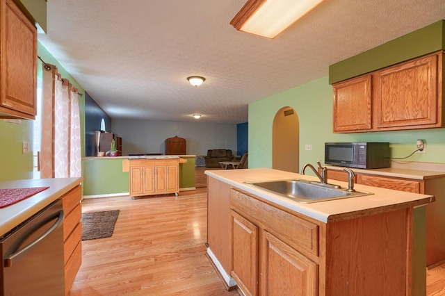 kitchen with a sink, a textured ceiling, open floor plan, stainless steel appliances, and light wood-style floors