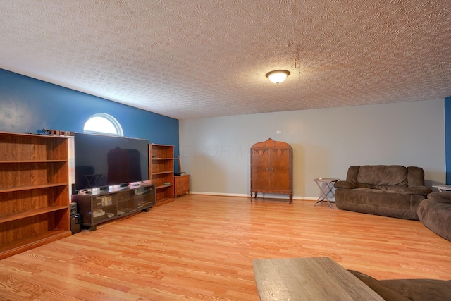 living room with a textured ceiling, light wood-type flooring, and baseboards