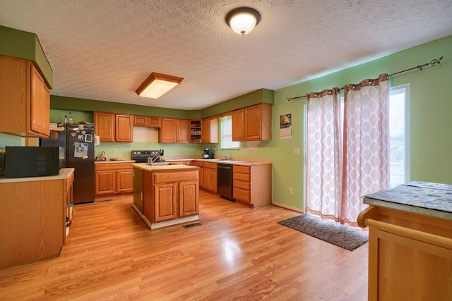 kitchen featuring visible vents, a center island with sink, light wood-type flooring, light countertops, and black appliances