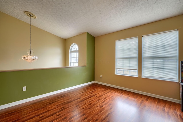 empty room featuring wood finished floors, baseboards, an inviting chandelier, vaulted ceiling, and a textured ceiling