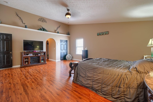 bedroom with a textured ceiling, wood finished floors, arched walkways, baseboards, and vaulted ceiling