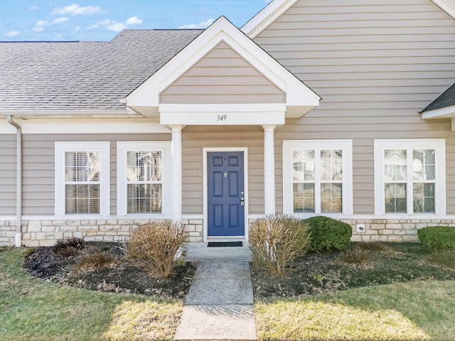 doorway to property with stone siding and a shingled roof