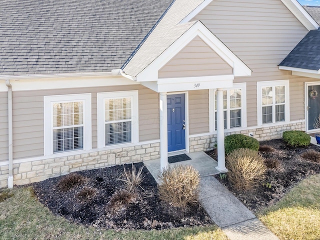 view of exterior entry with stone siding and a shingled roof