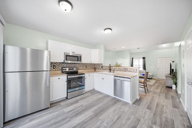 kitchen featuring light countertops, appliances with stainless steel finishes, a peninsula, white cabinetry, and a sink