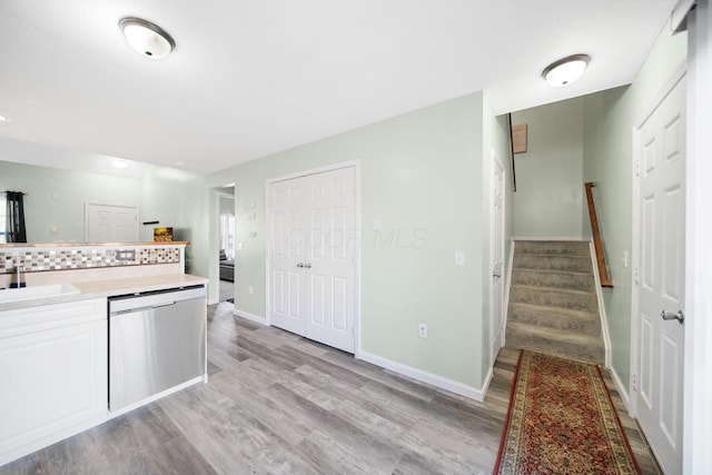 kitchen with light wood finished floors, dishwasher, light countertops, white cabinets, and a sink