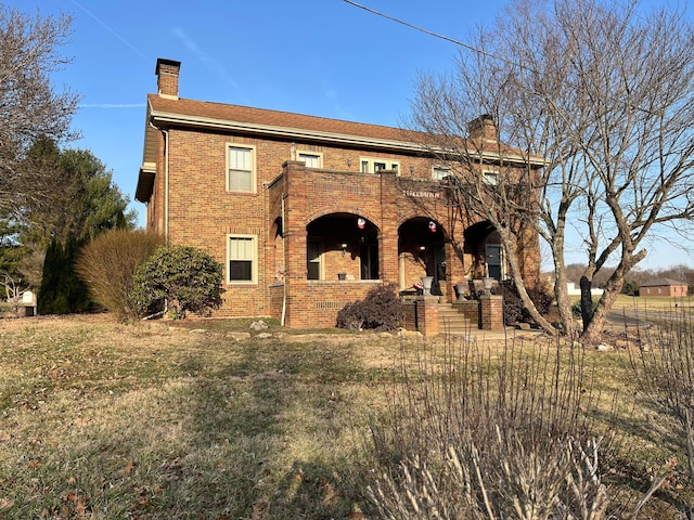 exterior space featuring a front yard, brick siding, a balcony, and a chimney