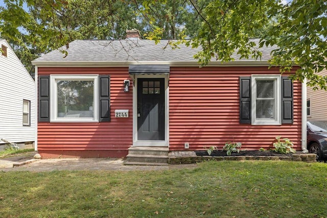 view of front of house featuring roof with shingles, a chimney, a front lawn, and entry steps