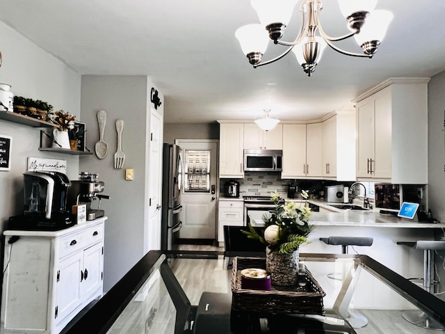 kitchen featuring a peninsula, a sink, decorative backsplash, stainless steel appliances, and white cabinetry