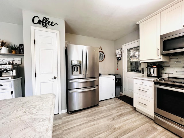 kitchen with light wood finished floors, white cabinetry, appliances with stainless steel finishes, and tasteful backsplash