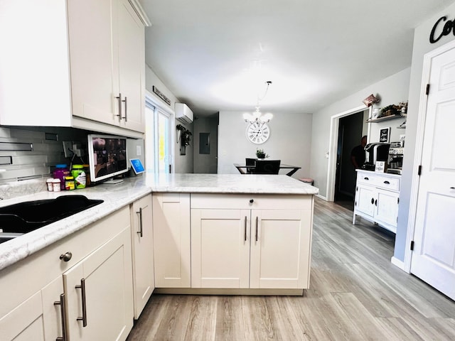 kitchen featuring light stone countertops, a wall mounted air conditioner, light wood-style flooring, a peninsula, and white cabinetry