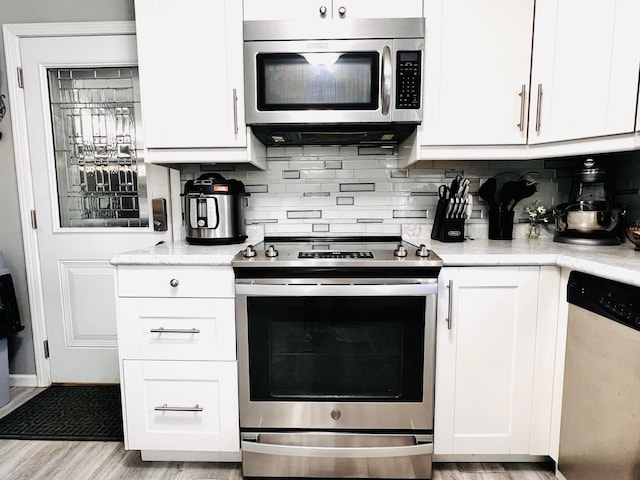 kitchen featuring stainless steel appliances, light wood finished floors, decorative backsplash, and white cabinetry