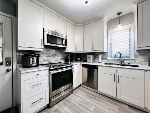 kitchen featuring tasteful backsplash, decorative light fixtures, appliances with stainless steel finishes, light wood-style floors, and a sink