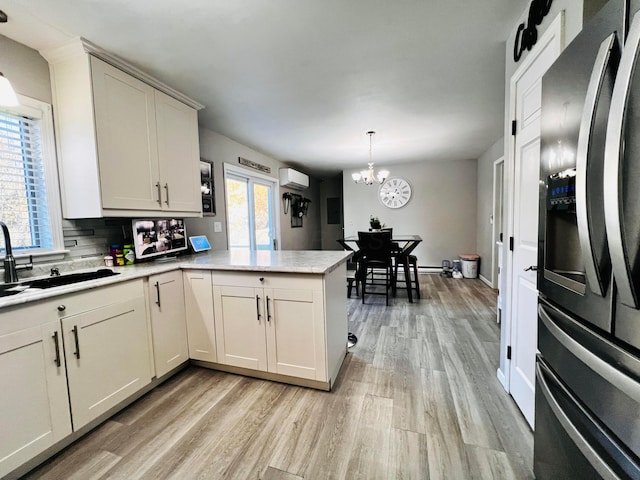 kitchen with a peninsula, stainless steel fridge with ice dispenser, a sink, an AC wall unit, and light wood-type flooring