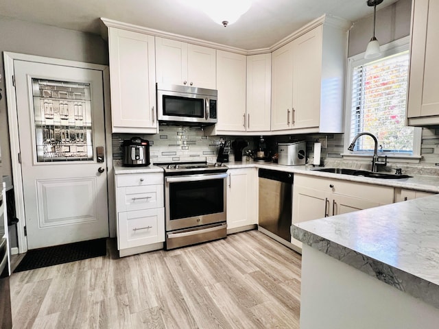 kitchen featuring light wood finished floors, pendant lighting, decorative backsplash, appliances with stainless steel finishes, and a sink