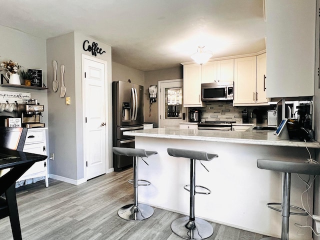 kitchen featuring light wood-type flooring, backsplash, appliances with stainless steel finishes, a breakfast bar area, and a peninsula