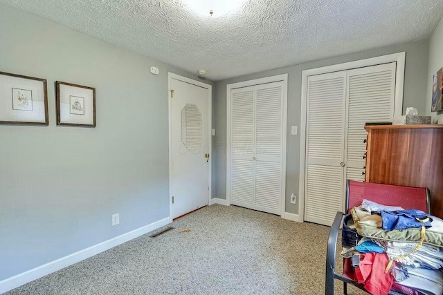 carpeted bedroom with baseboards, a textured ceiling, and multiple closets